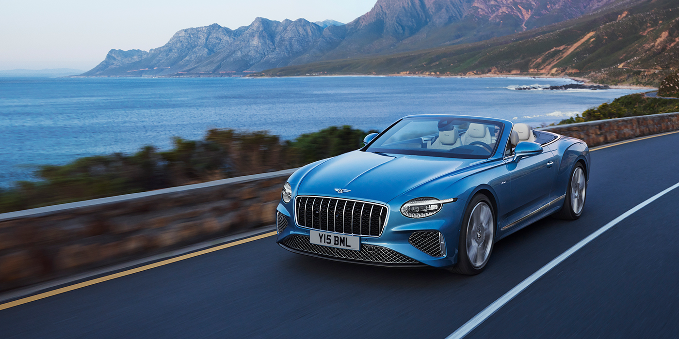 Bentley Madrid New Bentley Continental GTC Azure convertible in Light Windsor blue paint with 22 inch Azure wheels and chrome grill, driving dynamically by the sea