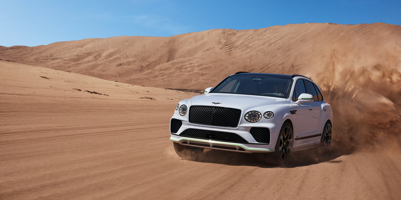 Bentley Madrid Bentley Bentayga Speed SUV front three quarter in Snow Quarts Pearlescent by Mulliner white paint driving dynamically through the desert
