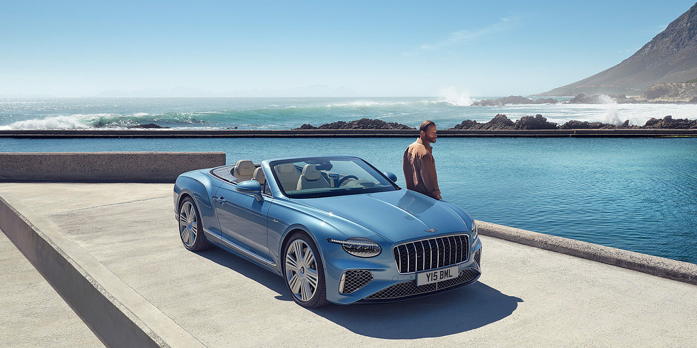 Bentley Madrid New Bentley Continental GTC Azure convertible front view in Light Windsor blue paint with 22 inch ten spoke wheels parked by the sea in the sunshine