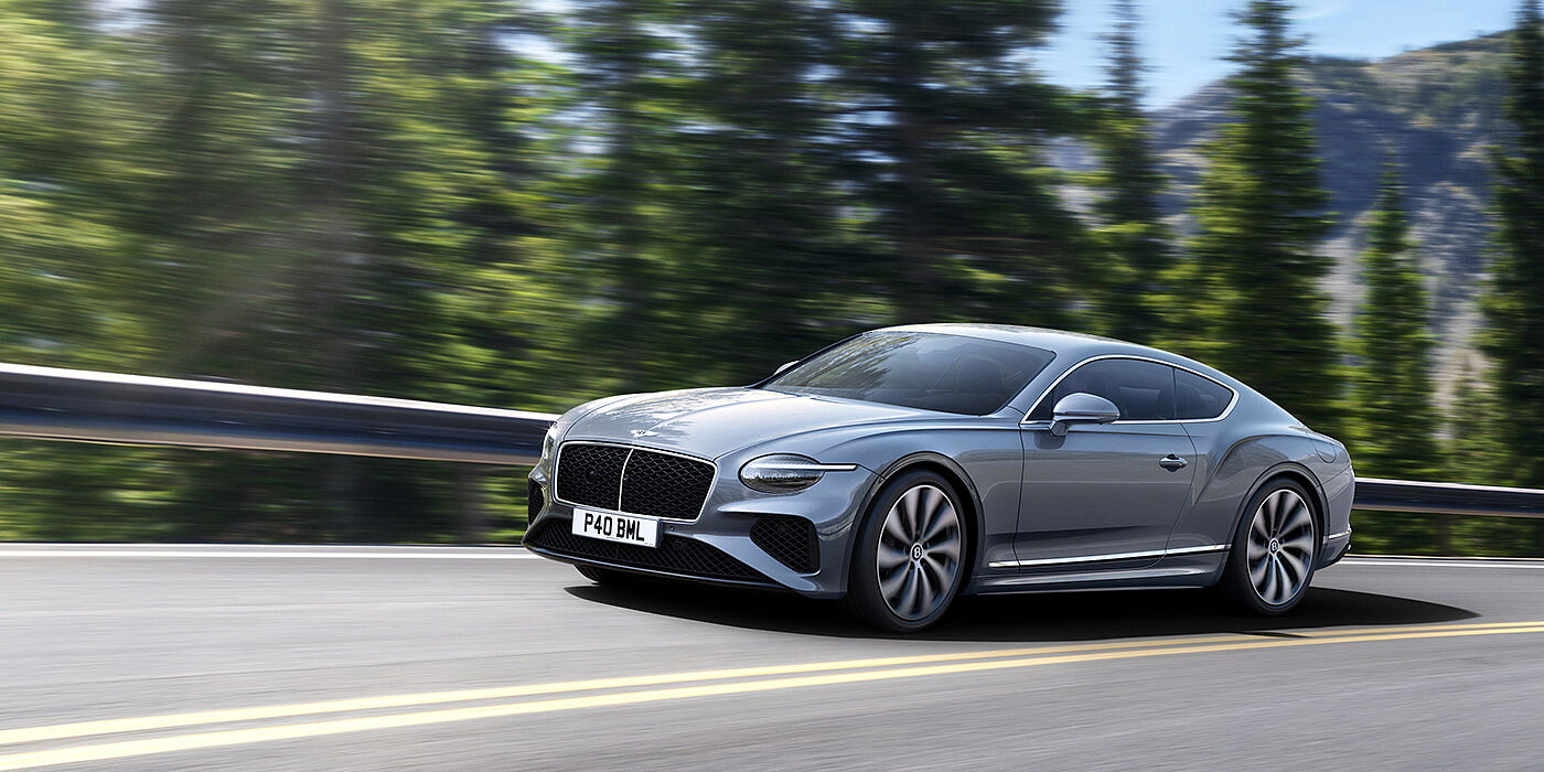 Bentley Madrid New Bentley Continental GT coupe in Silverlake paint and 22 inch ten-spoke wheels, driving dynamically on a tree-lined road in the sunshine