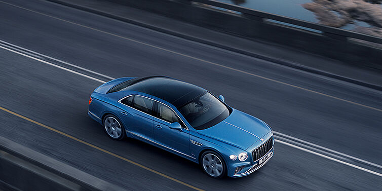 Bentley Madrid New Bentley Flying Spur Azure sedan in Light windsor blue paint by Mulliner, with 22 inch Azure wheels seen from overhead driving dynamically on a country road